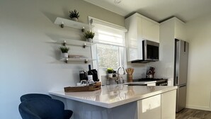 A modern kitchen with a central island, bar stools, a microwave, and a refrigerator.