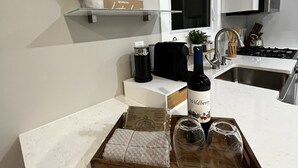 A modern kitchen with white cabinetry, a built-in oven, and a countertop with a tray holding a bottle of wine, glasses, and a box of Orville Redington wine.