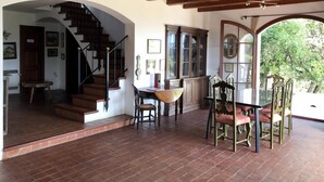 A spacious room with a wooden staircase, a dining area with a table and chairs, and a view of greenery outside. - Casa Illa Blanca, Aiguablava, Begur (Begur)