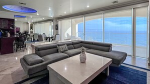 Ein modernes Wohnzimmer mit einem großen Ecksofa, einem Couchtisch und Blick auf den Ozean durch raumhohe Fenster.
