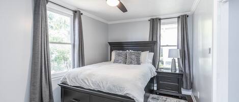 A bedroom with a bed, nightstands, a ceiling fan, and a window with curtains.