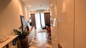Quarto de hotel moderno com padrão de piso em formato de losango, área de refeições com mesa e cadeiras, e uma grande planta em vaso.
