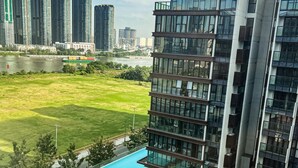 Um edifício moderno com piscina no terraço, rodeado por vegetação e vista para edifícios altos.
