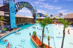 Relax by the pool surrounded by palm trees and lounge chairs, with a water slide and archway nearby.