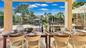 An outdoor dining area with tables set for six, surrounded by palm trees and a clear blue sky. - Natural Springs-2 acre, Games+karaoke, fit,views. (Riverside County)