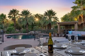 An outdoor dining area with a pool, palm trees, and a building in the background. - Natural Springs-2 acre, Games+karaoke, fit,views. (Riverside County)