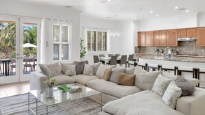 A modern living room with a sectional sofa, a glass coffee table, and a dining area with a kitchen in the background. - Natural Springs-2 acre, Games+karaoke, fit,views. (Riverside County)