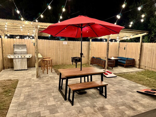Un patio al aire libre con una parrilla, muebles de madera y luces colgantes.