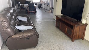 Un saló amb un sofà de pell marró, un moble de televisió de fusta i una zona de menjador al fons.