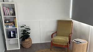 Una habitació amb un rug amb textura circular, una cadira de fusta, una taula rodona petita, una estanteria i un aire condicionat fixat a la paret.