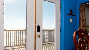 A room with a large sliding glass door leading to a balcony with a wooden railing. The room has a blue wall and a patterned floor. - 10M From the Ocean! Upper Suite with Amazing Views - Highest Tides in the World (Five Houses)