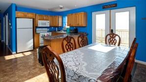 A kitchen with wooden cabinets, a white refrigerator, a microwave, and a dining area with a table covered by a lace tablecloth. - 10M From the Ocean! Upper Suite with Amazing Views - Highest Tides in the World (Five Houses)