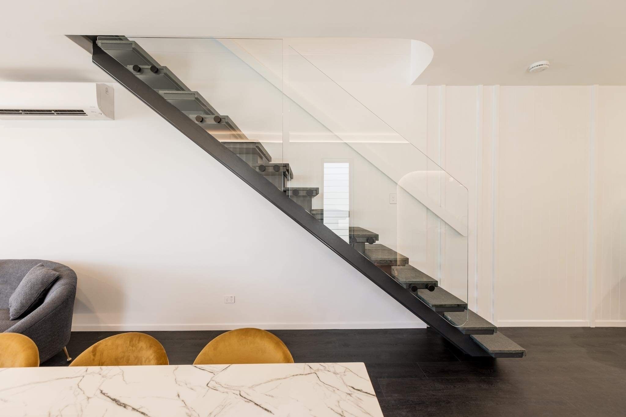 Un interior moderno con una escalera de cristal, una mesa de mármol y un sofá.