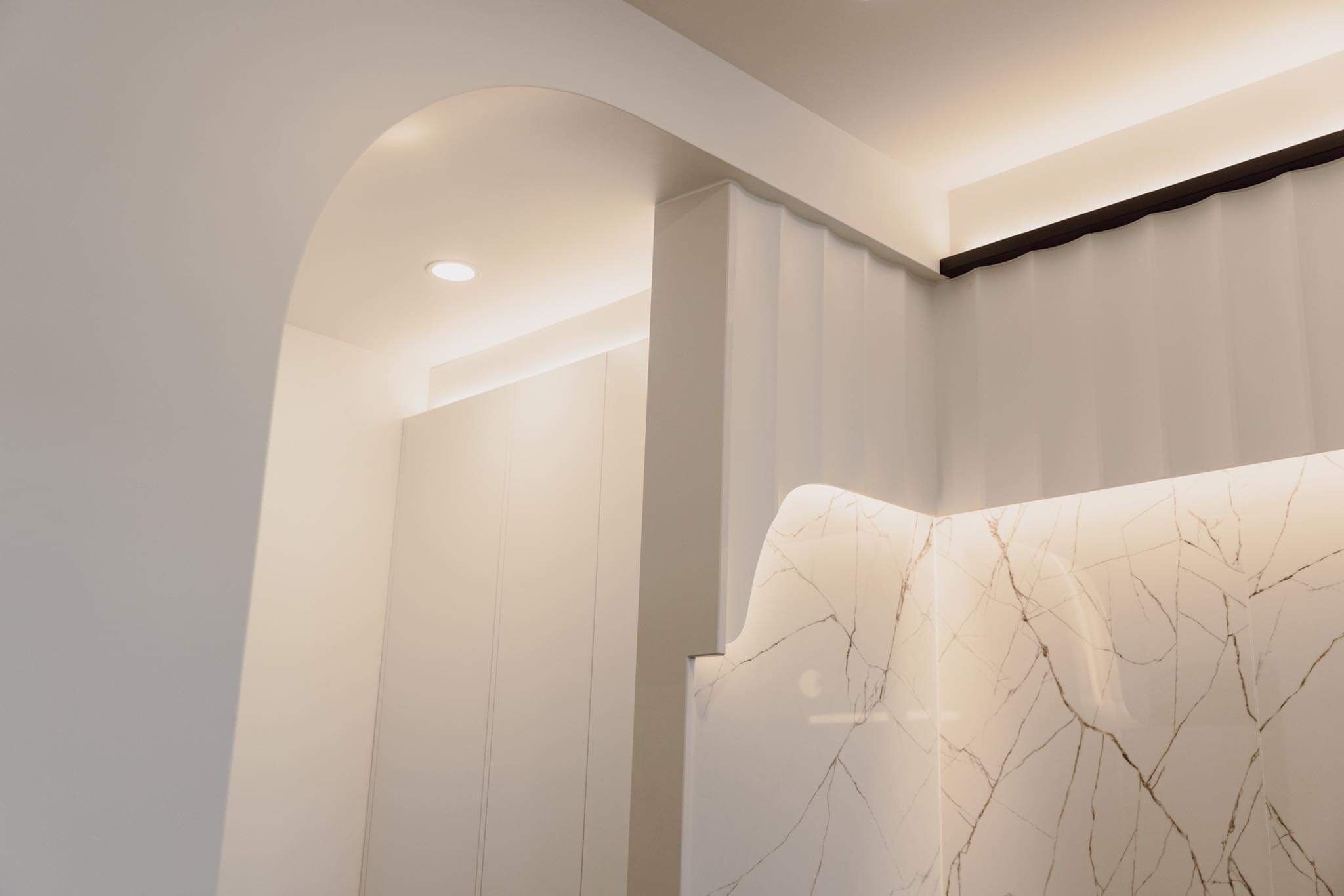 A modern bathroom with a marble vanity, recessed lighting, and a curved archway.
