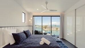 Een moderne slaapkamer met een groot bed, een plafondventilator en uitzicht op een meer en bergen.