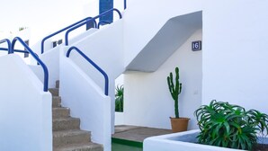 Ein weißes Gebäude mit einer Treppe und einem blauen Geländer. An der Wand ist die Hausnummer 16 angebracht.