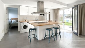 Eine moderne Küche mit einer zentralen Kochinsel, Barhocker, einer Waschmaschine und Blick ins Freie.