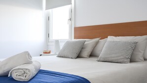 Ein ordentlich bezogenes Bett mit blauer Bettdecke und weißen Kissen, ein Holz-Kopfteil und ein Nachttisch mit Kerze und einer kleinen Dekoration.