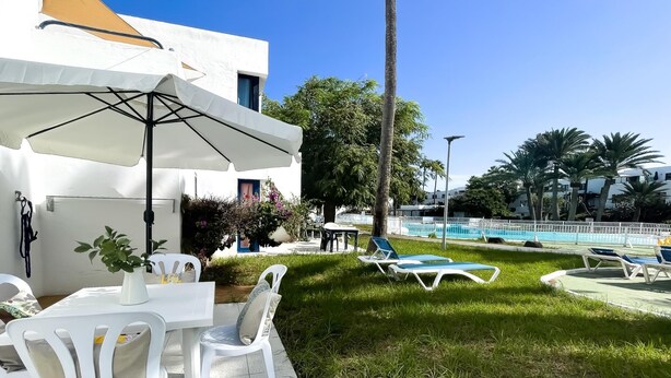 Ein Außenbereich mit weißen Tischen und Stühlen, einem Pool und Palmen.