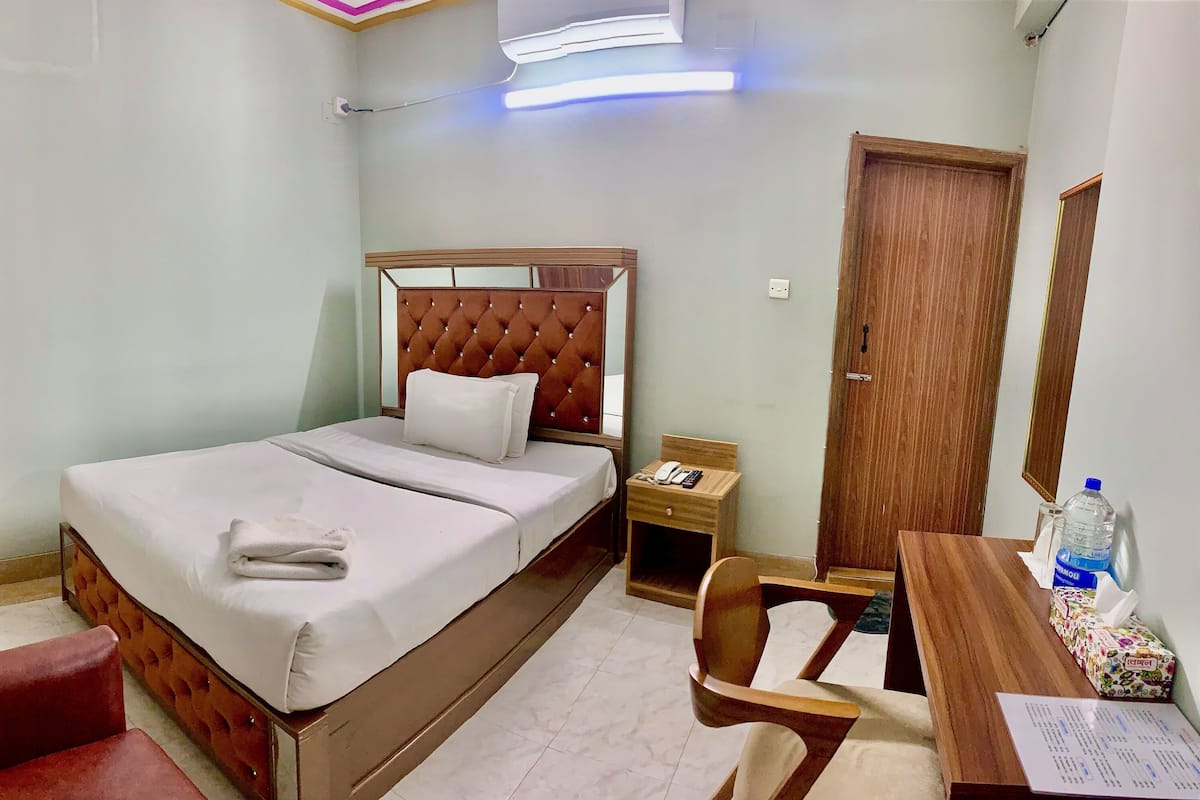 A neatly arranged hotel room with a bed, a desk, a chair, a wardrobe, and a television.