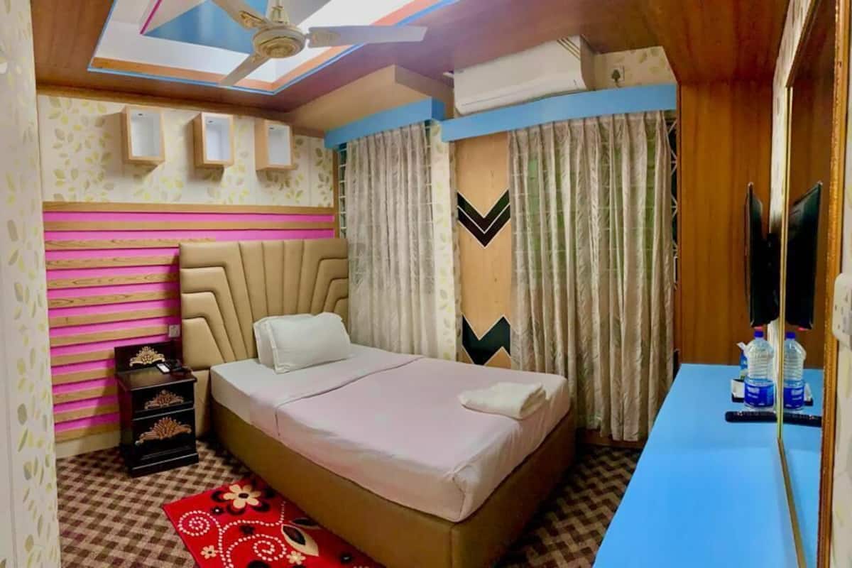 A bedroom with a bed, a desk, a ceiling fan, and a window with curtains.