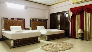 Quarto de hotel com duas camas, ventoinha no teto, ar condicionado, um espelho grande e cortina vermelha.