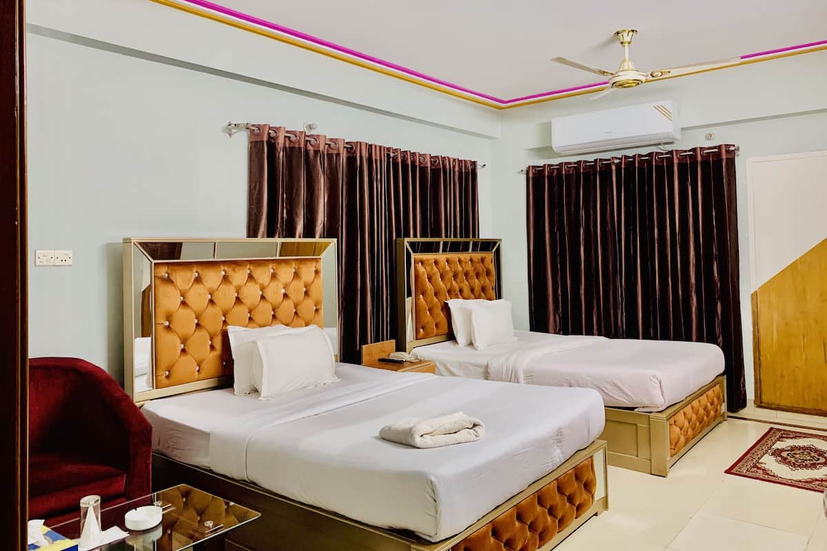 A hotel room with two beds, a red chair, a glass table, and a ceiling fan.