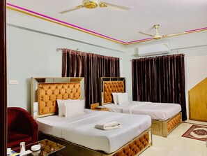 A hotel room with two beds, a red chair, a glass table, and a ceiling fan. - Heaven Inn (Dhaka)