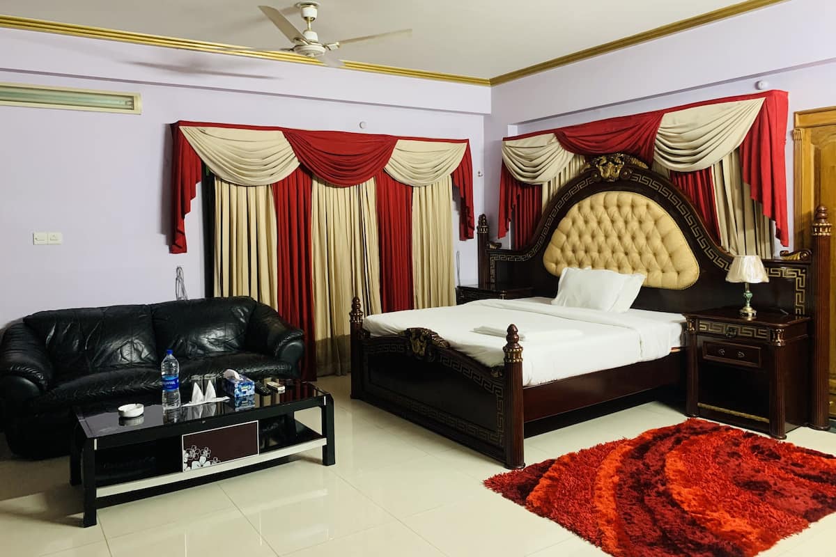 A bedroom with a bed, a black leather sofa, a coffee table, and a red rug.