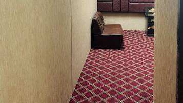 A narrow room with a patterned carpet, a cushioned bench, and a wall-mounted panel.