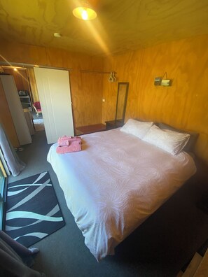 A bedroom with a large bed, a mirror, a wardrobe, and a small seating area. - Toddy’s Batch (Glenorchy)