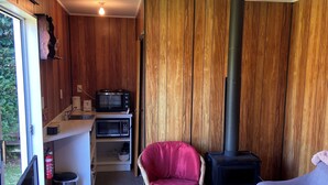 Un espace de vie compact comprenant un coin cuisine, une chaise rouge, un canapé et un mur lambrissé.