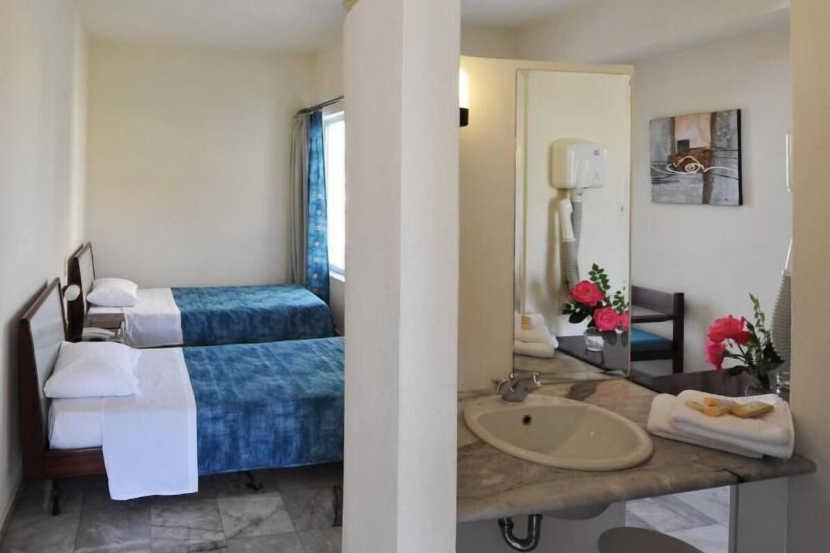 Ein Hotelzimmer mit zwei Betten, einem Badezimmer mit Waschbecken, Spiegel und einem Bild an der Wand.