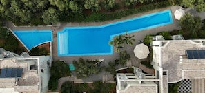Luftaufnahme eines Resorts mit zwei Schwimmbecken, einer überdachten Terrasse und einem Gebäude mit Solarpanels.