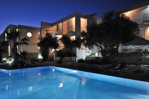 Un bâtiment moderne doté d’une piscine, d’un espace extérieur aménagé et d’une façade bien éclairée.
