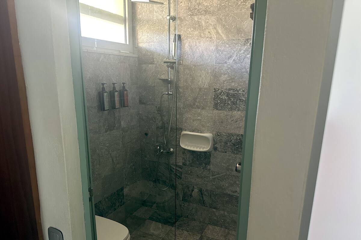 Eine Duschkabine mit Glaswänden, eine Toilette und ein Seifenspender an der Wand.