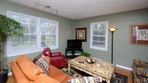 A living room with a brown leather sofa, a red leather chair, a coffee table with decorative items, and a television on a stand. - State Line Rd near Downtown Q39 BBQ-KUMC. WESTPORT! (Kansas City)