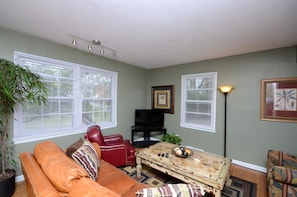 A living room with a brown leather sofa, a red leather chair, a coffee table with decorative items, and a television on a stand.