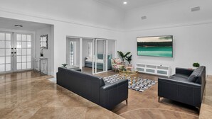 Un salón amplio con techo alto, un ventanal grande y un televisor de pantalla plana montado en la pared.