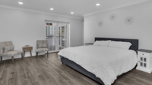 Un dormitorio con una cama grande, dos sillas, una mesita de noche y una puerta que da a un balcón.