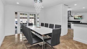 Una cocina moderna con armarios blancos, una isla central y una zona de comedor con mesa blanca y sillas negras.
