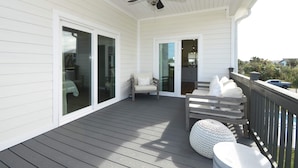 A covered deck with a ceiling fan, a chair, a sofa, and a round ottoman. - Beachwalk Luxury Home: Heated Pool & Free Bikes (Palm Coast)