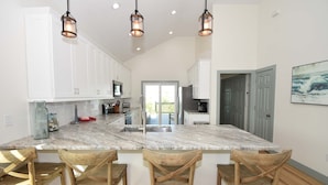 A kitchen with a marble island, wooden chairs, white cabinets, and pendant lighting. - Beachwalk Luxury Home: Heated Pool & Free Bikes (Palm Coast)