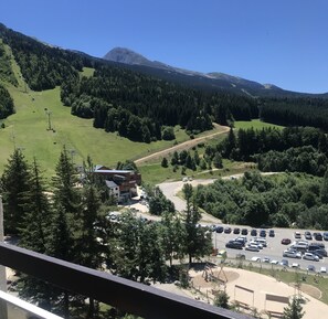 A mountain view with a ski lift, a parking area, and a building with a sign. - Studio at the foot of the slopes (Villard-de-Lans)
