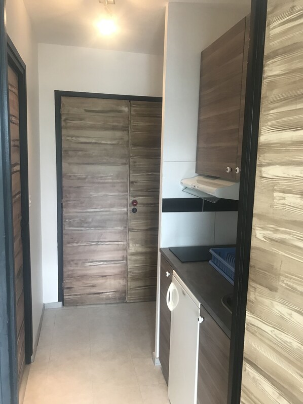 A compact kitchen with a wooden door, a washing machine, and a countertop with a sink. - Studio at the foot of the slopes (Villard-de-Lans)