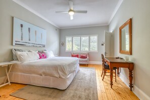 Ein Schlafzimmer mit Bett, Schreibtisch, Stuhl, Deckenventilator und einem Fenster mit Jalousien.