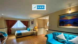 A hotel room with a bed, a blue sofa, a small table with a lamp, and a painting on the wall. - S79 Vuon Saigon Hotel & Spa (Ho Chi Minh City)