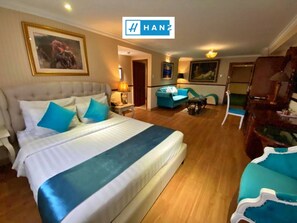 A hotel room with a large bed, a sofa, a desk, and a chair. There is a painting on the wall and a lamp on the desk. - S79 Vuon Saigon Hotel & Spa (Ho Chi Minh City)