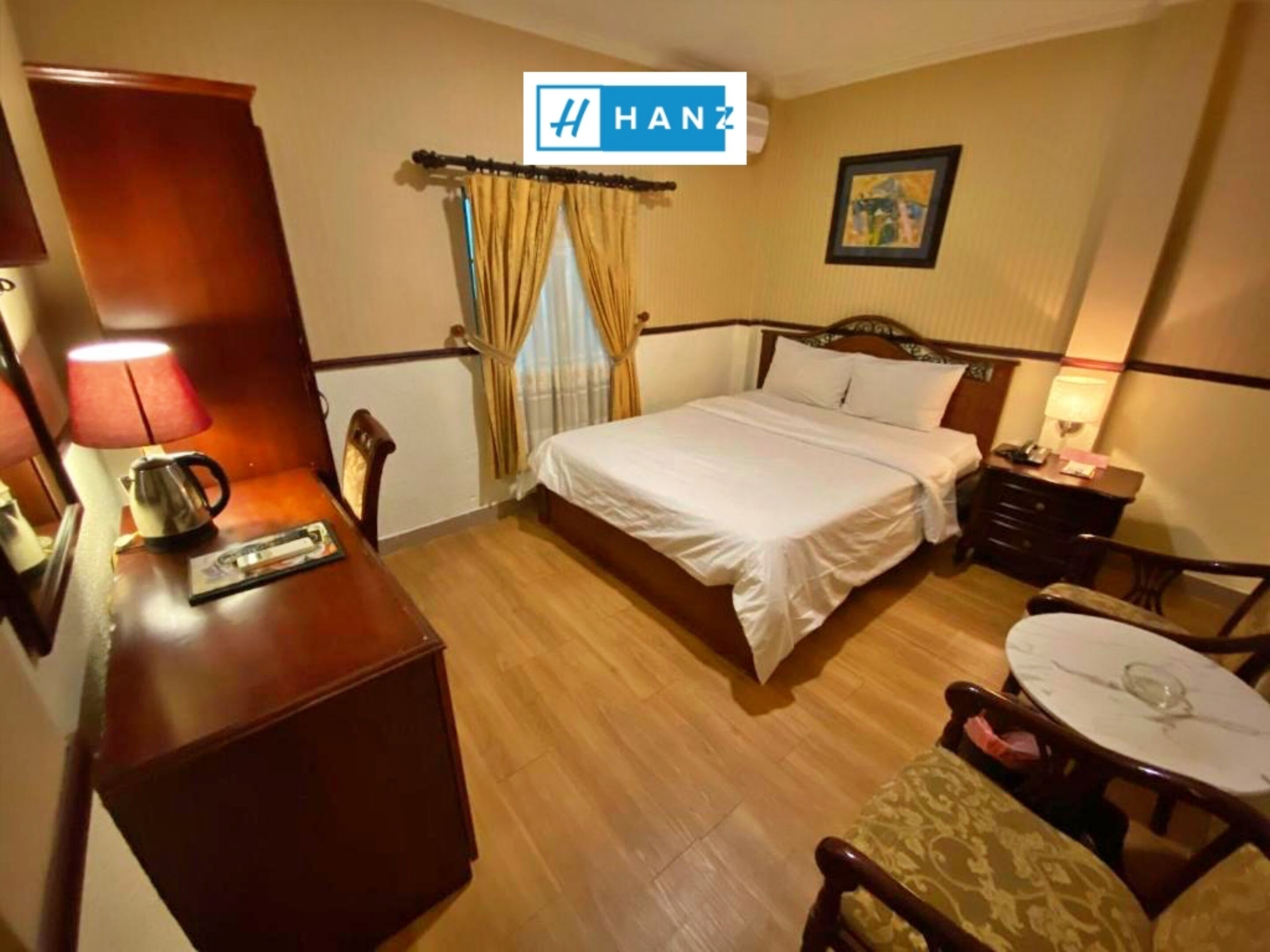 Una habitación de hotel con cama, mesita de noche, lámpara y una pequeña mesa con una silla.