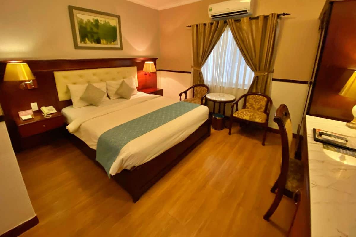 Quarto de hotel com cama, mesas de cabeceira, escrivaninha, cadeira e ar condicionado.
